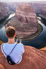 Mann sitzt am Horseshoe Bend mit Ausblick auf den Grand Canyon