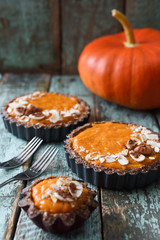 Autumn pies. Vegetarian pumpkin tartlets with nuts and oats on shabby blue background served with raw pumpkin