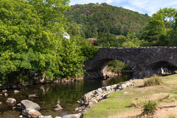 Fototapeta premium Old stone bridge over River Duddon in Ulpha in the Lake District National Park, UK. Scenic view of English countryside on a sunny day
