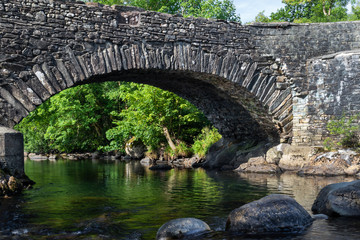 Old stone bridge over River Duddon in Ulpha in the Lake District National Park, UK. Scenic view of English countryside on a sunny day