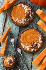 Autumn dessert. Vegetarian pumpkin tartlets with nuts and oats on shabby blue background with raw pumpkin