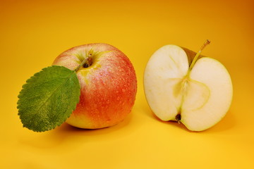 Red apple with green leaf and cut apple half on yellow background
