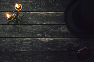 Bowler hat, wallet, rusty key and burning candle on wooden table background.