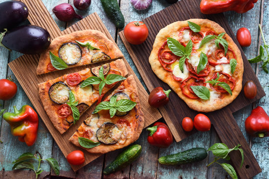 Healthy vegetarian food. Pizzas with eggplants, tomatoes and bell peppers on oak boards served with raw vegetables on shabby blue background
