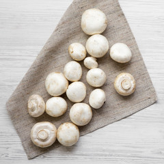 Champignon mushrooms on cloth on white wooden table, top view. From above, overhead. Close-up.