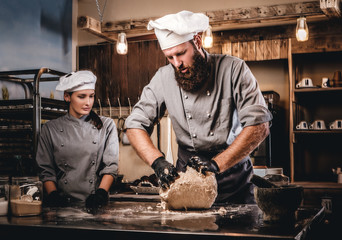 Chef kneading dough in the kitchen. Chef teaching his assistant to bake the bread in the bakery.