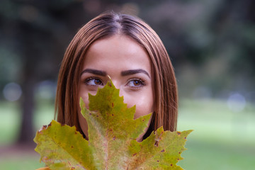 Young girl brown eyes hiding behind a leaf in an autumn day