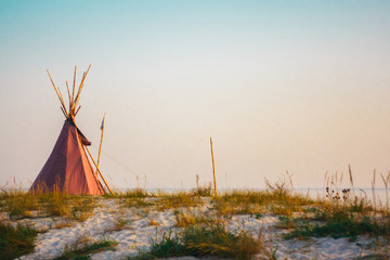 Red wigwam on the sandy seashore. Indian native national building outdoors summer. Teepees on coast.