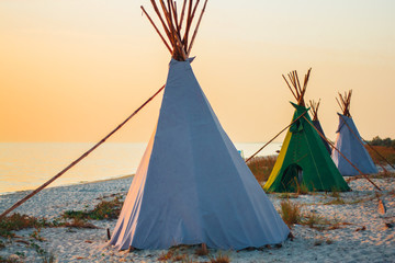 Wigwams on the sandy seashore. Indian native national building outdoors summer. Teepees on coast.