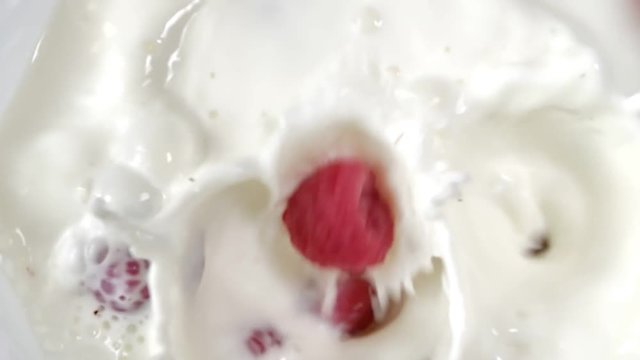 Top view slow motion fresh juicy berries falling into white milk or yogurt close-up