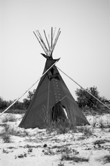 Black wigwam on sandy seashore. Native american indian building outdoors in summer. Teepee in grayscale © baklykovadaria