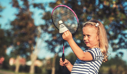 Childhood time. Beautiful little girl playing badminton in the park