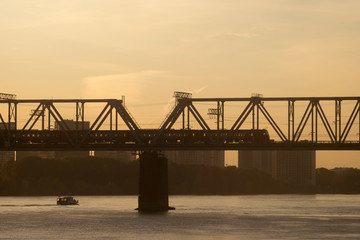 The train goes under the river over the railway bridge. Silhouetee photo at the sunset