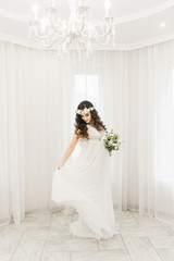 Attractive young pregnant girl in a white dress with curls, a wreath and a bouquet of flowers. Photo session waiting for the baby