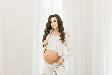 Stylish young pregnant girl in white clothes with curls and naked . Photo session waiting for the baby