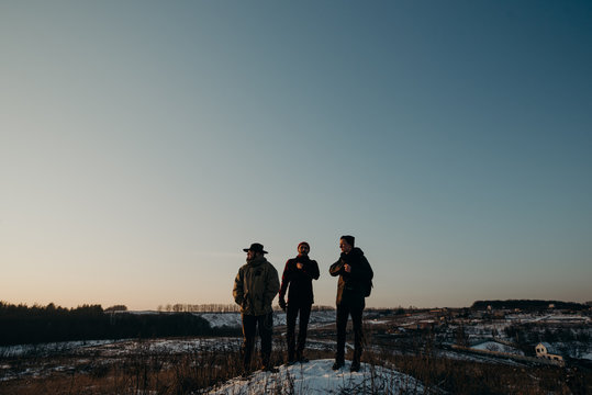Four friends stand on a hill during a beautiful sunset. Winter trip. Relax and meeting friends. Friendship and longevity.