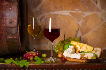Red and white wine with  grapes beside old cask in wine cellar. Glasses and bottles of wine with cheese and nuts on wooden table. horizontal