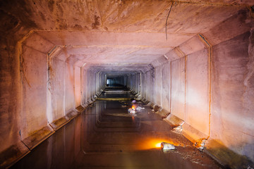 Flooded rectangular sewer tunnel with dirty urban sewage illuminated by color lights and candles 