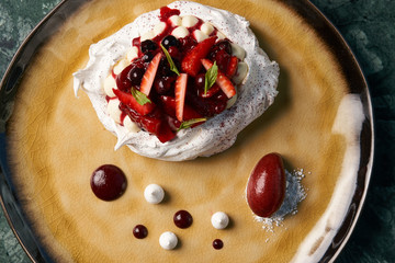 Homemade Pavlova fruit cake and berry ice cream dessert on wooden table background, close-up