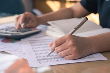 Business concep : close up woman hand using calculator and holding pen and pointing paper chart business report on office desk.