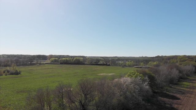 Flying over feald and trees, train moving to the left in distance. Drone track shot.