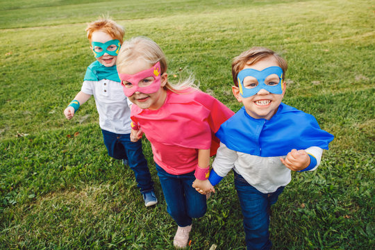 Cute adorable preschool Caucasian children playing superheroes. Three kids friends having fun together and running outdoors in park. Happy active childhood and friendship concept.