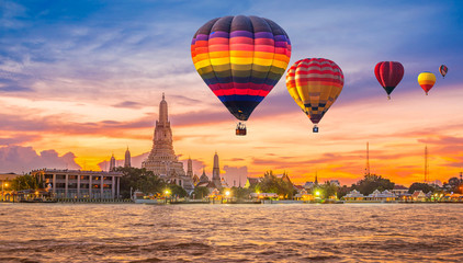 Colorful hot air balloons flying over Chao Phraya River near Wat Arun Temple at twilight in Bangkok, Thailand