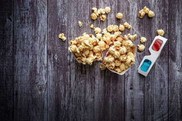 Cinema background, top view.  Popcorn and 3D glasses on wooden table. Movie accessories, cinematography concept, flat lay