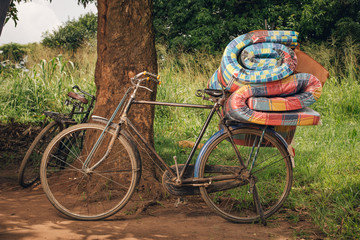 African bike with rolled beds on the back lays against a tree, ready to be ridden back to the nearby village.