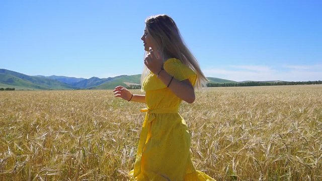 A young girl in a yellow dress with long hair running on a wheat field. Slow motion. HD