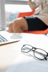 Closeup of elegant black rim glasses lying over documents on table in office lit by sunlight, copy space