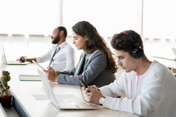 Obraz premium Portrait of three young people sitting in row and using gadgets at work in open office, copy space