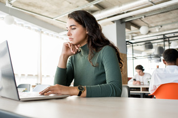 Portrait of pensive young woman using laptop while working in open office, copy space