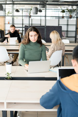 Portrait of young woman using laptop at desk while working in open space office of modern company