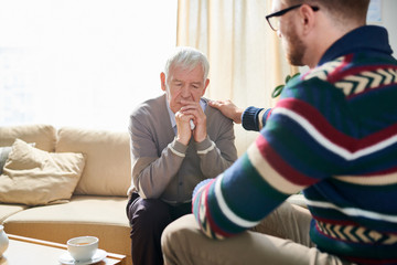Back view portrait of male psychologist consoling depressed senior man during therapy session, copy...