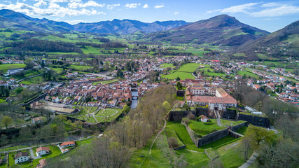 Aerial panorama view of Saint Jean Pied de Port, a fortified military town in the Pyrenees along the el camino de santiago, with blue sky abd lush green pasture. Star shaped Vauban fort. - obrazy, fototapety, plakaty