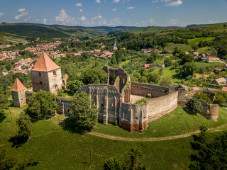 Fototapeta na wymiar Aerial view of ruined Gothic Saxon medieval Slimnic castle near Sibiu, Romania with donjon, church, barbican, walls on a green hill with blue cloudy sky