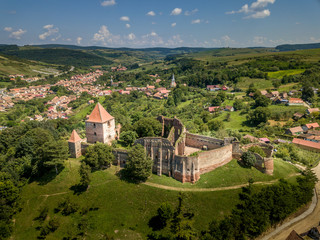 Fototapeta na wymiar Aerial view of ruined Gothic Saxon medieval Slimnic castle near Sibiu, Romania with donjon, church, barbican, walls on a green hill with blue cloudy sky