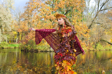 charming fairy of autumn in the yellowed forest stands on the shore of the forest lake with her...