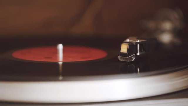 An old, dusty record player is playing a black vinyl record with a red label at 33 1/3 rpm. The record player is in a wooden cabinet.