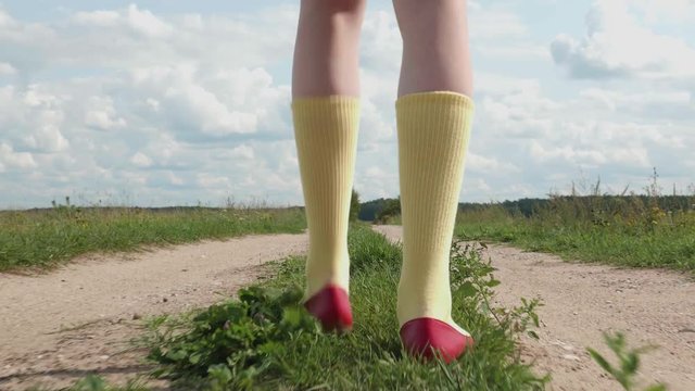 TRACKING SHOT: This is a PART of several clips where you can see A Pair Of Red Shoes And Yellow Socks Walking On Different Surfaces. In this video, we see them WALK ON THE PATH
