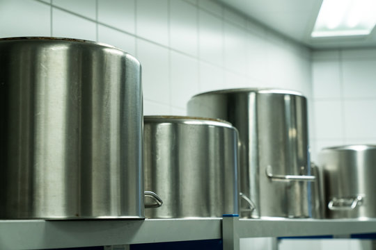 row of large metal cooking pots in an industrial size restaurant kithcen on a metal shelf