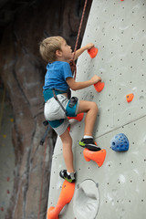 Fototapeta premium Young boy climbing up an indoor wall at the rock climbing gym