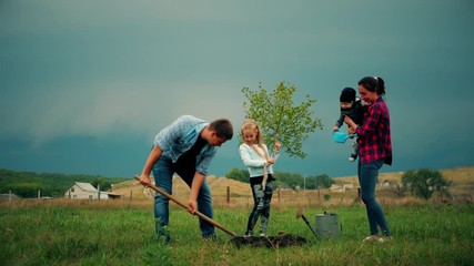 Family of four planting a new tree in his garden. The concept is to plant trees, a friendly family.