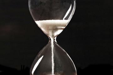 A closeup of an hourglass with falling sand, on a dark background with copy space