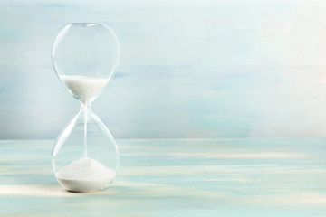A side view of an hourglass with falling sand, on a teal background with copy space