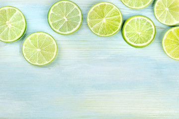 An overhead photo of many vibrant lime slices on a teal blue background