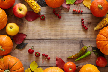 Naklejka na ściany i meble Thanksgiving background. Autumn harvest on the wooden table. Ripe pumpkins, corn, zucchini, tomatoes, apples, pepper and autumn colorful leaves forming frame. 