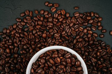 White cup full of with roasted brown coffee beans on the black concrete stone background. Flatlay style.