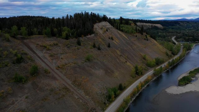 A cinematic aerial view of some steep cut-bank cliffs and road at dusk. Featuring the Prince George cut-banks and Nechako river.